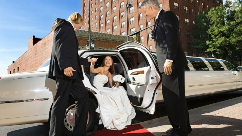The bride, driver and the groom with a white limousine.