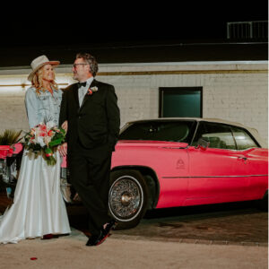 A beautiful couple posing for a photo with a pink limousine at the backdrop