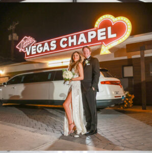 Bride and groom smiling for a photo in front of The Little Vegas Chapel and a white limousine