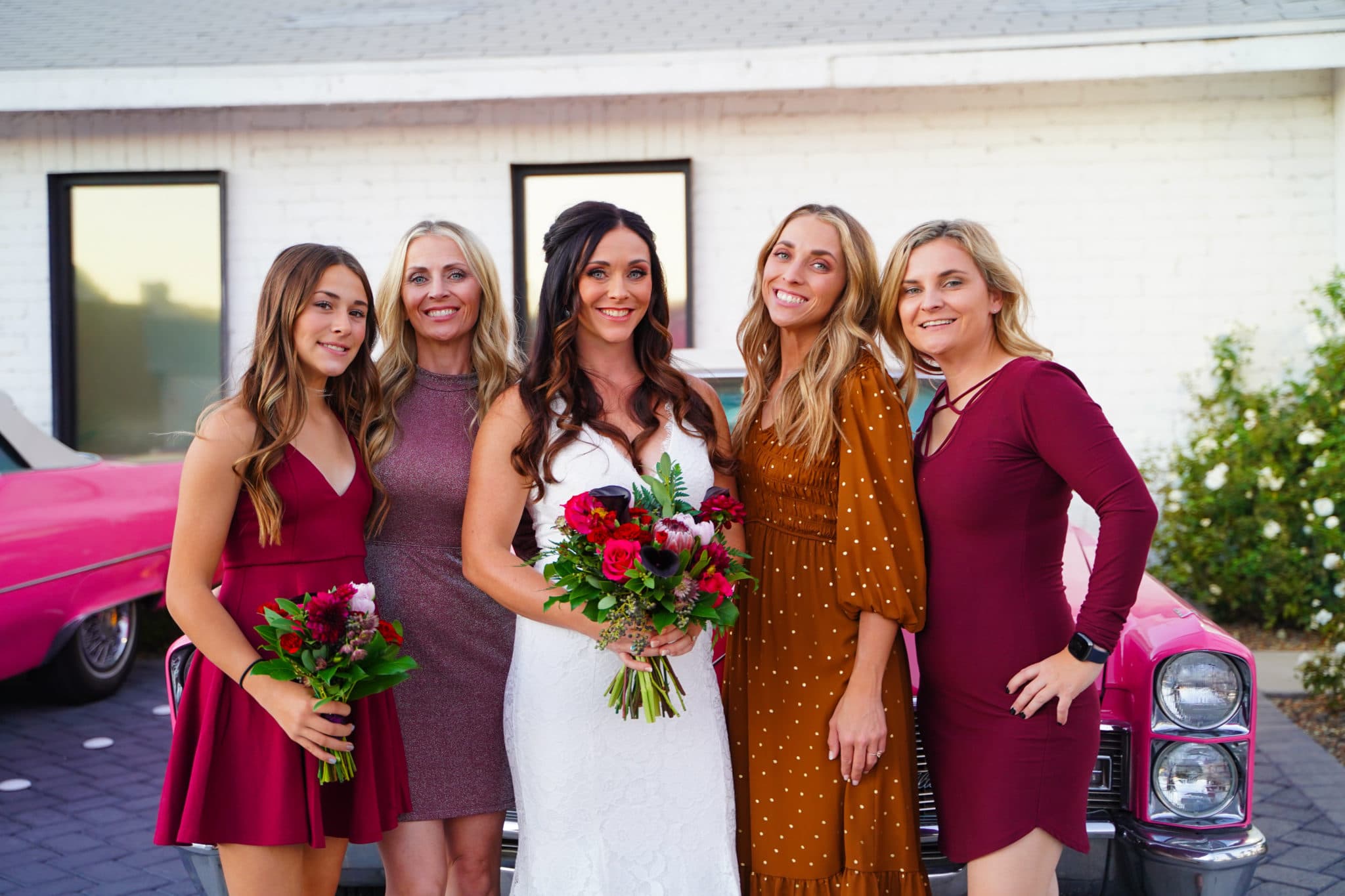 Bridal Party of five stands in front of Pink Cadillacs looking into the camera.