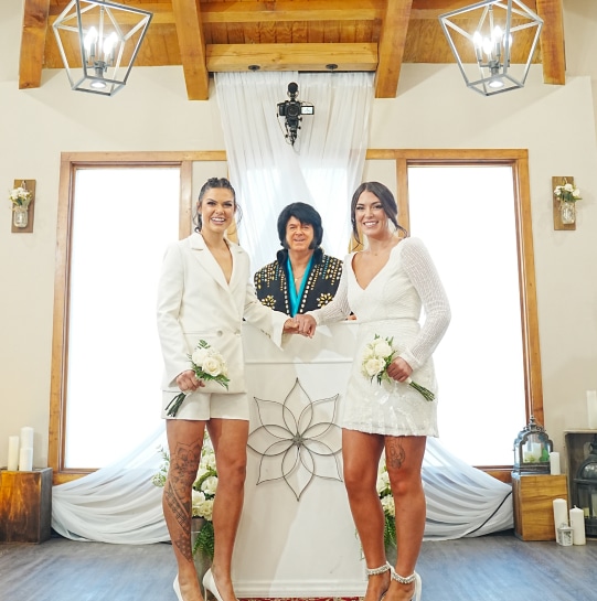 two women holding hands in front of an altar with Elvis Presley officiator