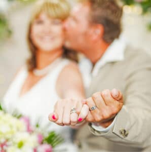 An out of focus image of bride and groom displaying their wedding rings