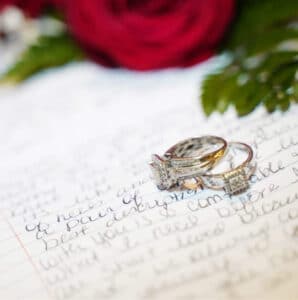 Two rings on top a note with red rose in the background symbolizing vow renewals